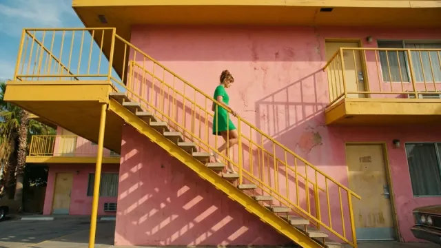 A woman in a green dress on a yellow staircase against a pink motel wall